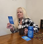 Janny is sitting at her kitchen table with a cup of coffee whilst reading a card from the CBT Deck. Link below.